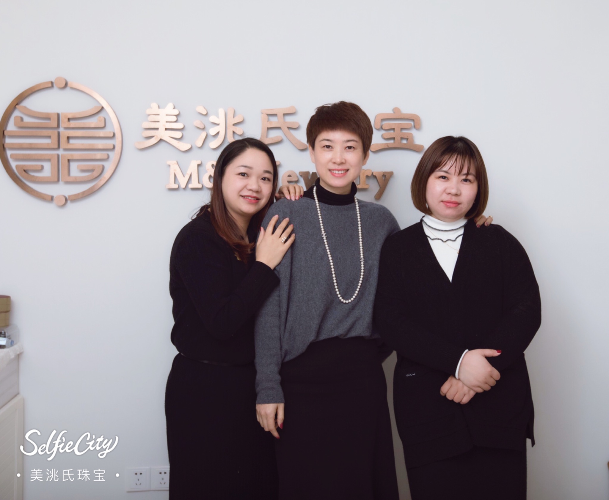The three women behind M&T Jewelry together in front of the original gold brand sign